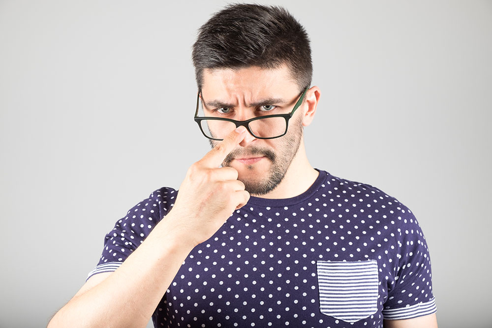 Un uomo con espressione infastidita spinge in su con il dito gli occhiali da vista che scivolano sul naso.