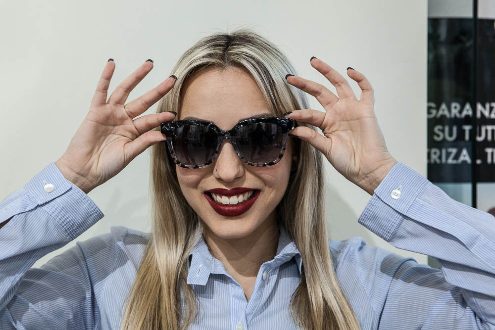 Ragazza felice e sorridente che indossa occhiali da sole con lenti polarizzate per combattere la fotofobia, all'interno di Pielle Centro Ottica a Monserrato.